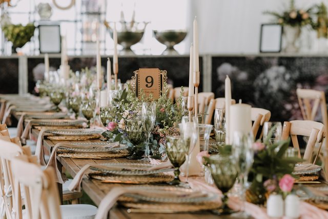 Farm table set with gold chargers, glassware, candles and greenery