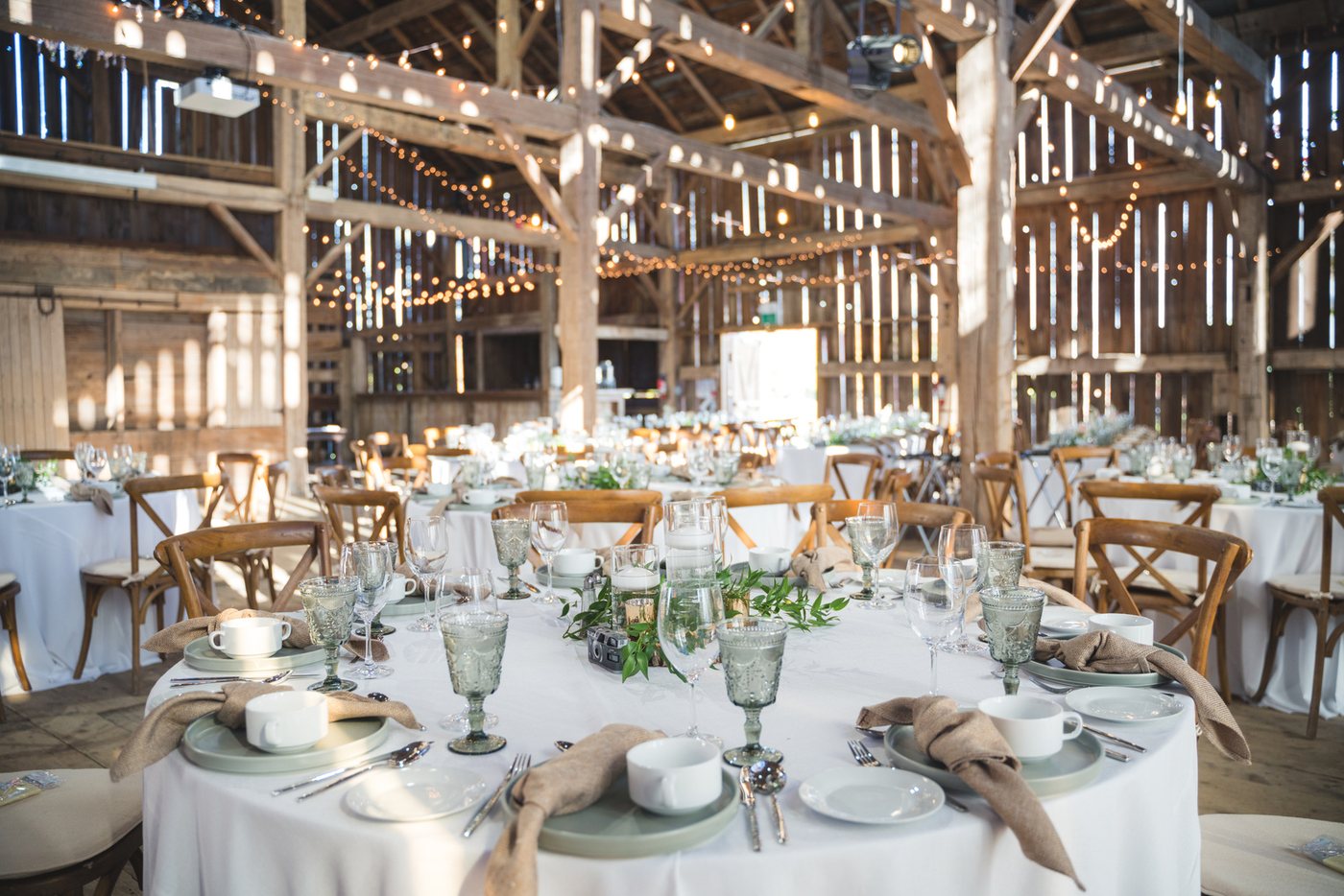 Barn wedding reception with round tables, linens and string lighting